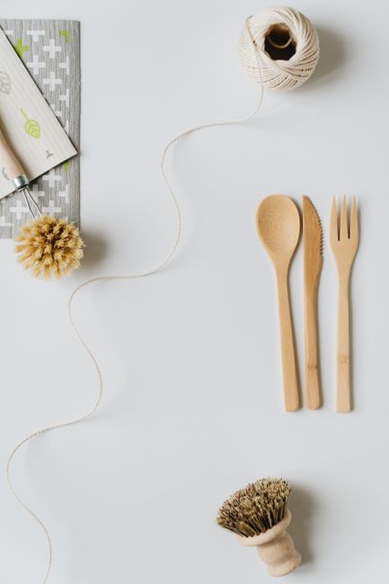 A ceramic bowl with a matte grey finish is placed on top of a folded white cloth and a larger beige cloth, situated on a crumpled light beige fabric surface. A natural wooden-handled cleaning brush wi